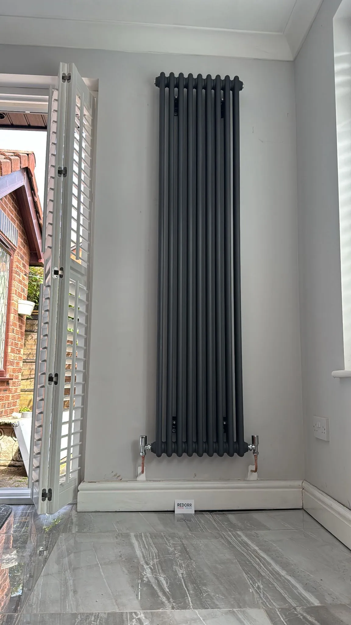 A tall vertical anthracite designer radiator installed by Redorr Heating & Cooling Services Ltd in a modern room in Warrington.