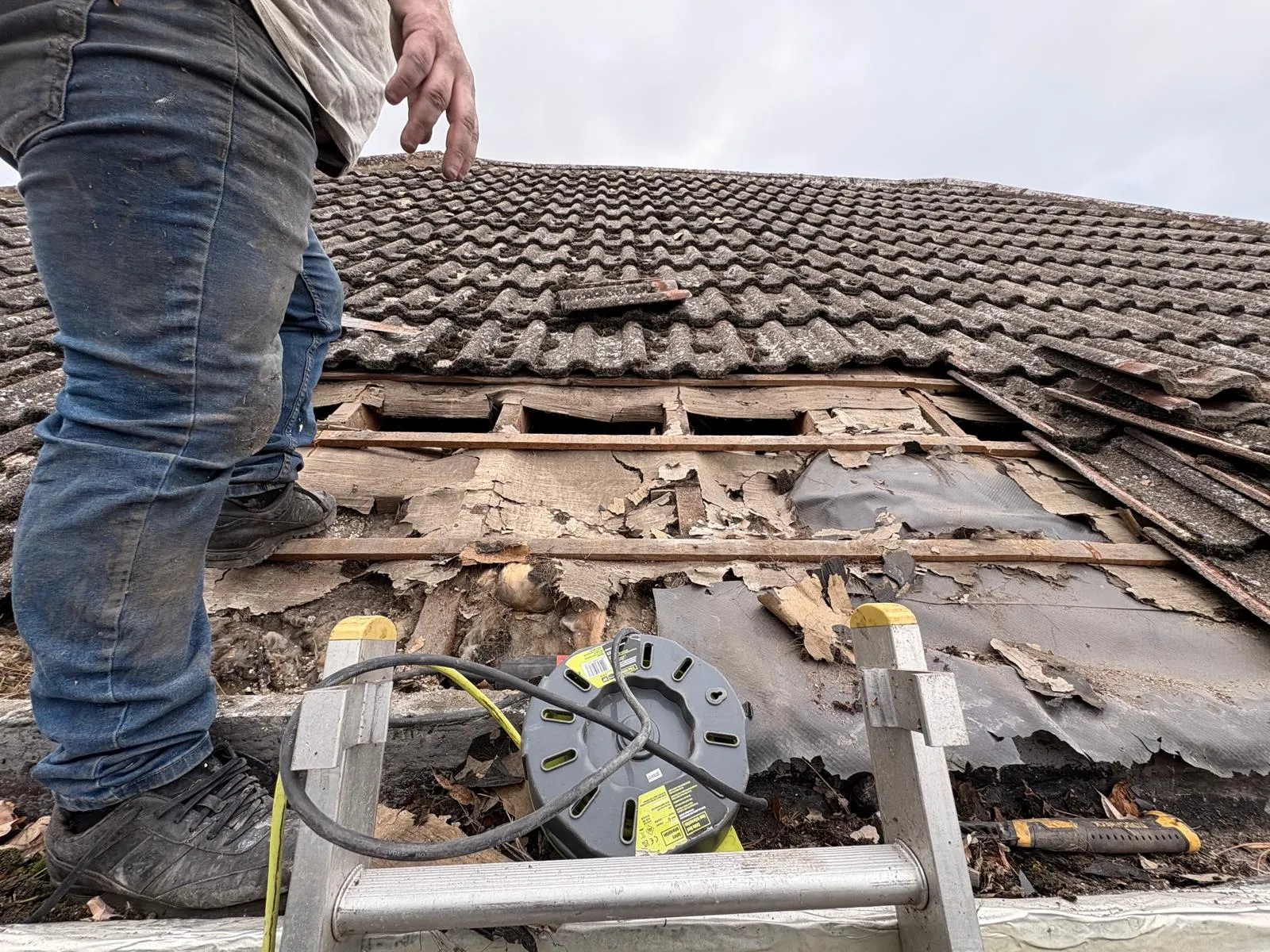 Tiled roof repair showing exposed rotted timber battens and deteriorated underlay beneath concrete tiles
