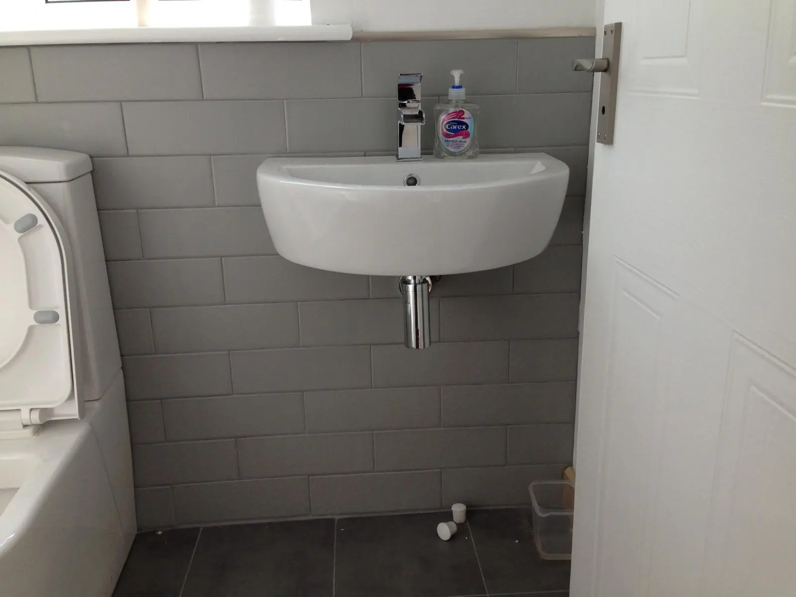 Modern bathroom plumbing installation featuring a wall-hung sink and grey tiling by MK Plumbing LTD.