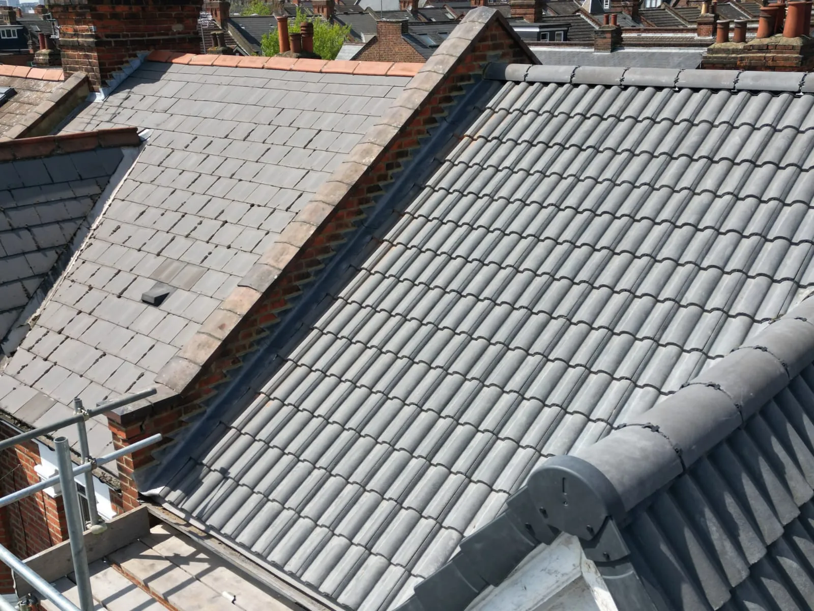 A close-up view of a newly installed or renovated pitched roof with two types of grey tiles, showing detail of the roofing materials and a valley.