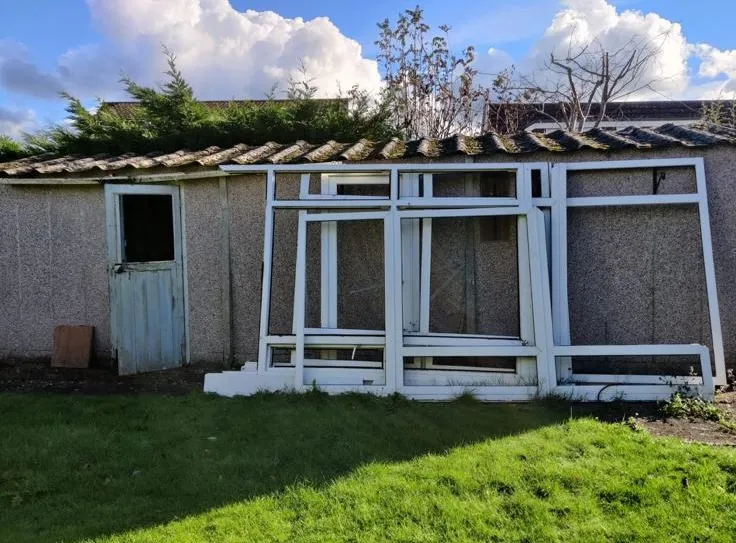 An old concrete garage with a corrugated asbestos roof in a garden