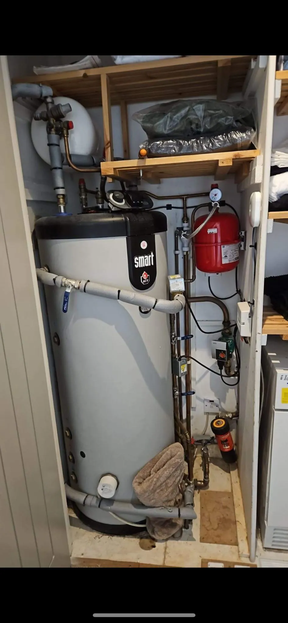 An unvented hot water cylinder with red expansion vessel inside domestic airing utility cupboard