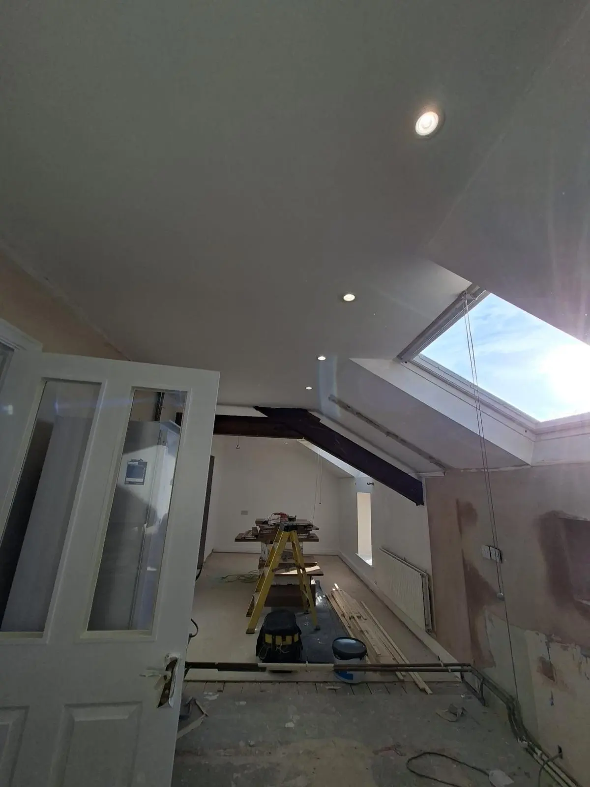 High-end interior renovation in progress showing a skylight, exposed wooden structural beam, and newly plastered ceiling.