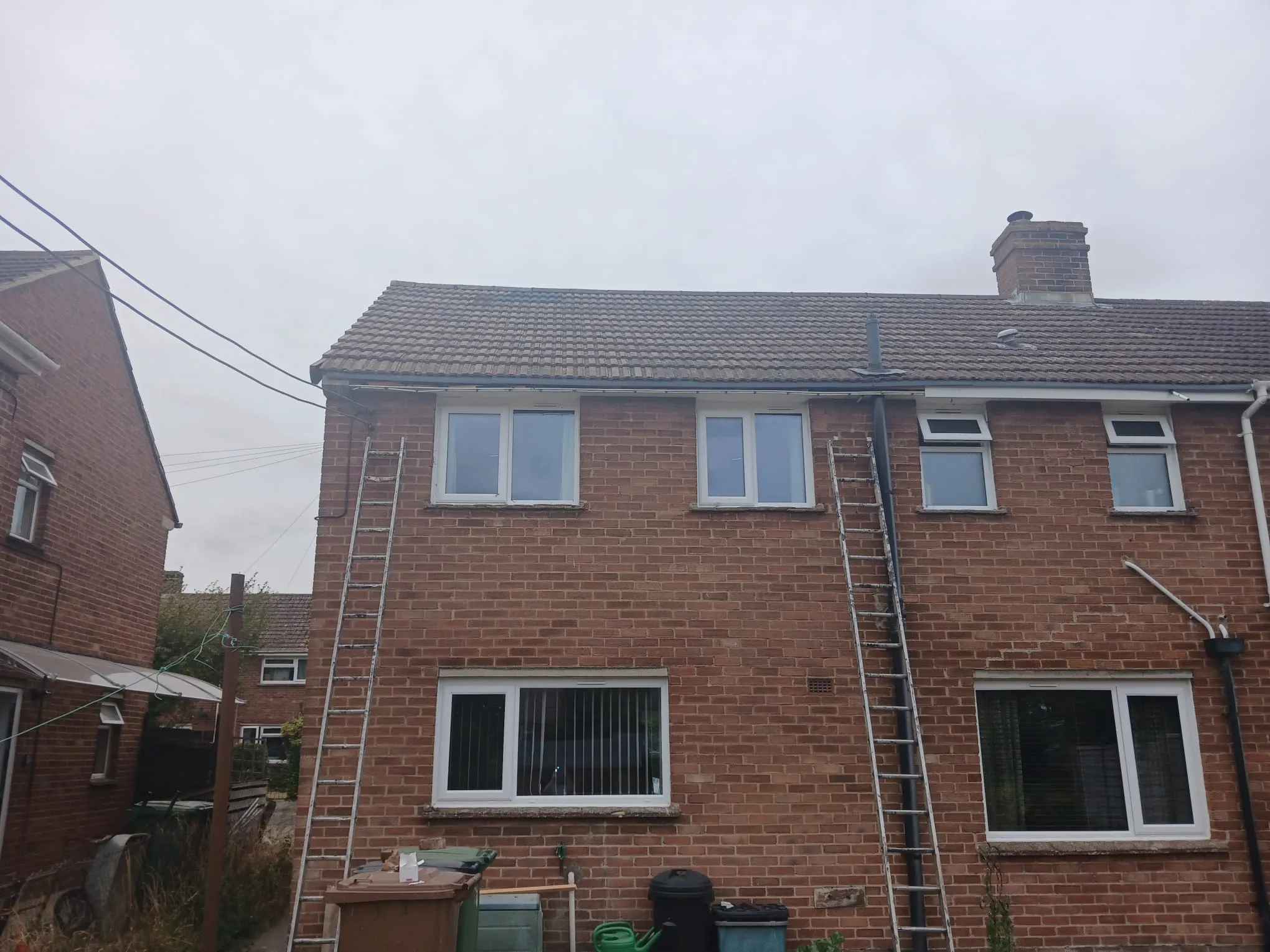 Ladders set up along the roofline and gutters of a brick residential house for maintenance work