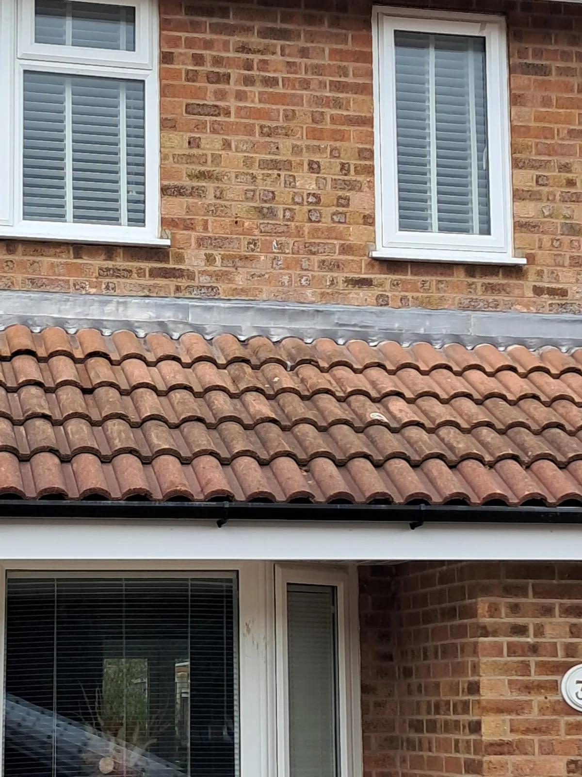 Close-up of a residential roof with traditional red clay tiles, lead flashing, and new black guttering on a brick property in Leicestershire.
