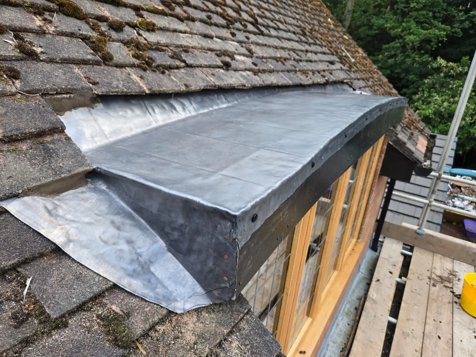 Close-up of a new flat roof installation with lead flashing connecting to an existing tiled pitched roof.