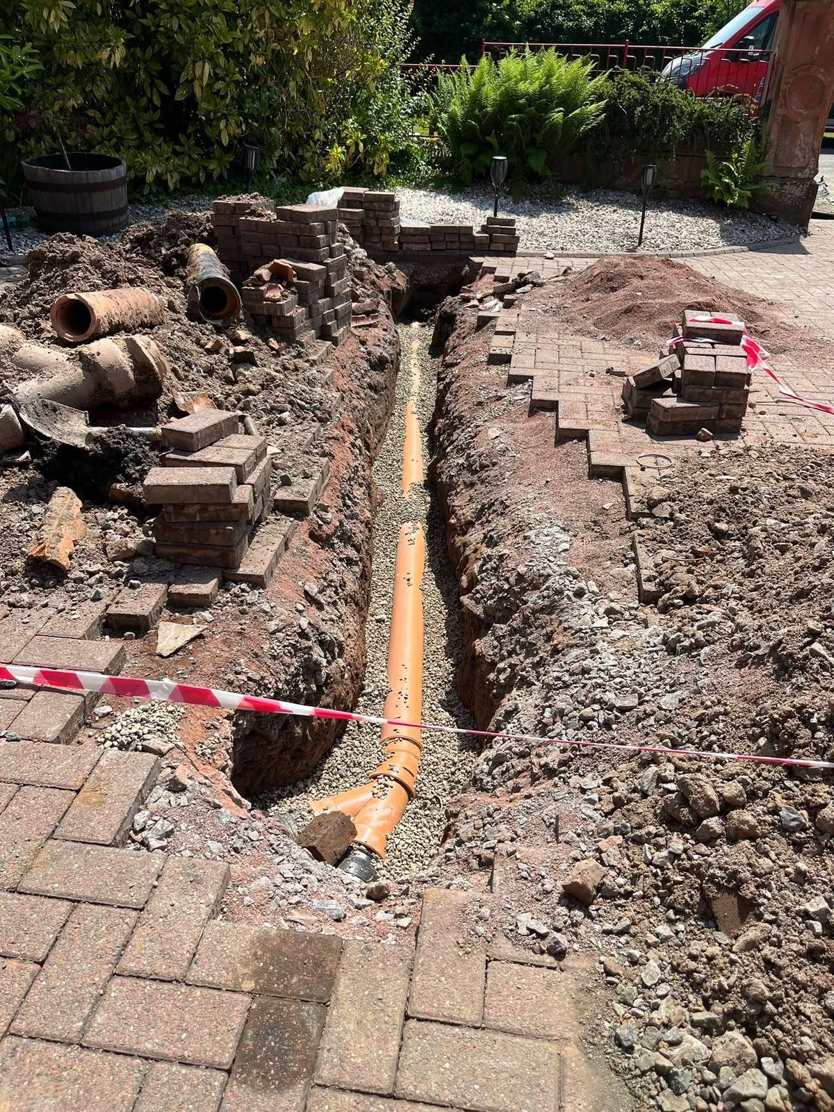 Newly installed orange drainage pipe in an excavated driveway trench during a drain pipe replacement project by CB Drainage.