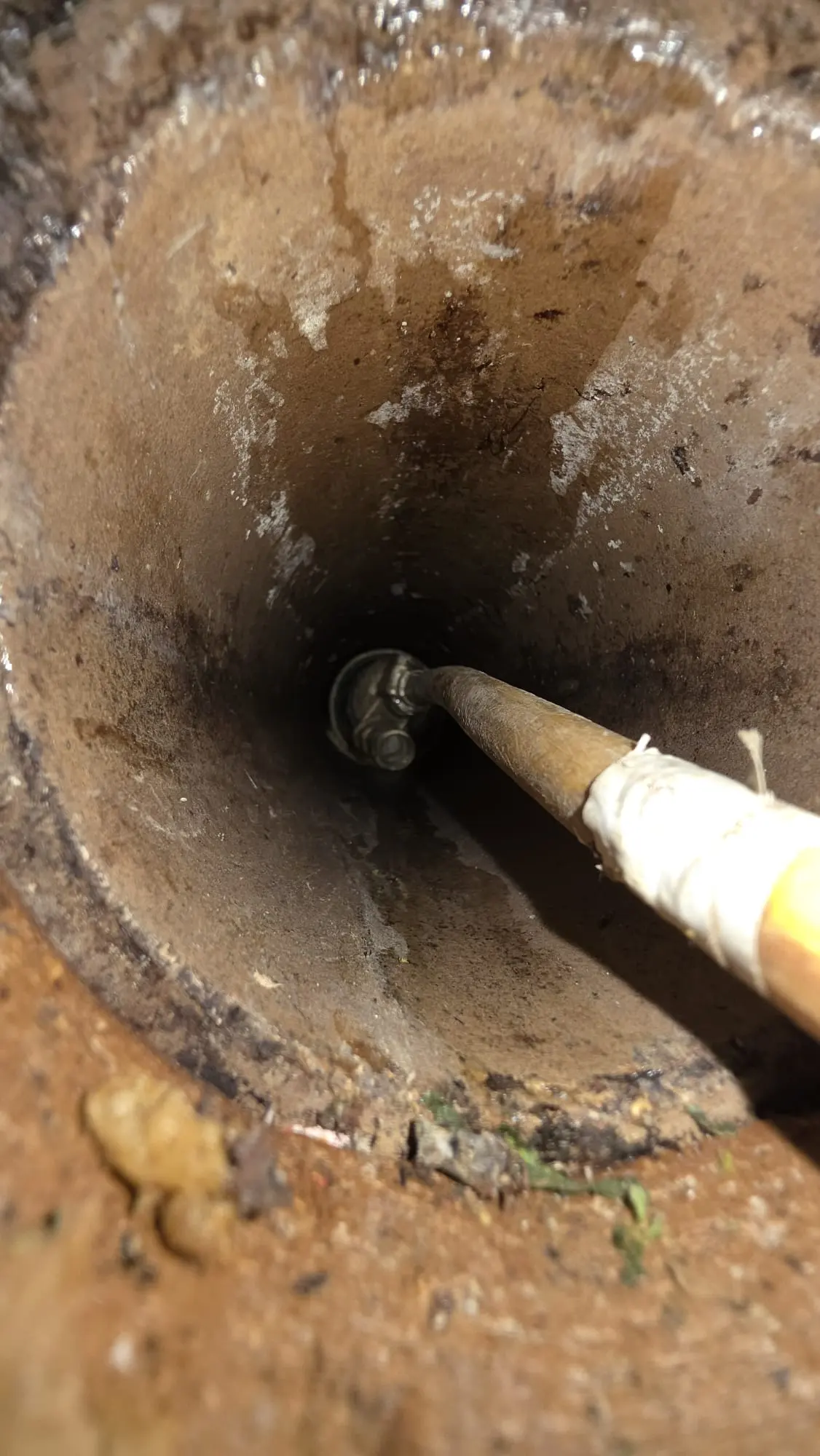 Internal view looking down an aged drain pipe with a cleaning hose or rod inserted, demonstrating drain unblocking techniques.
