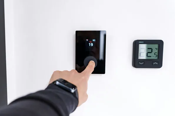 A homeowner adjusting a smart heating thermostat to improve domestic energy efficiency.