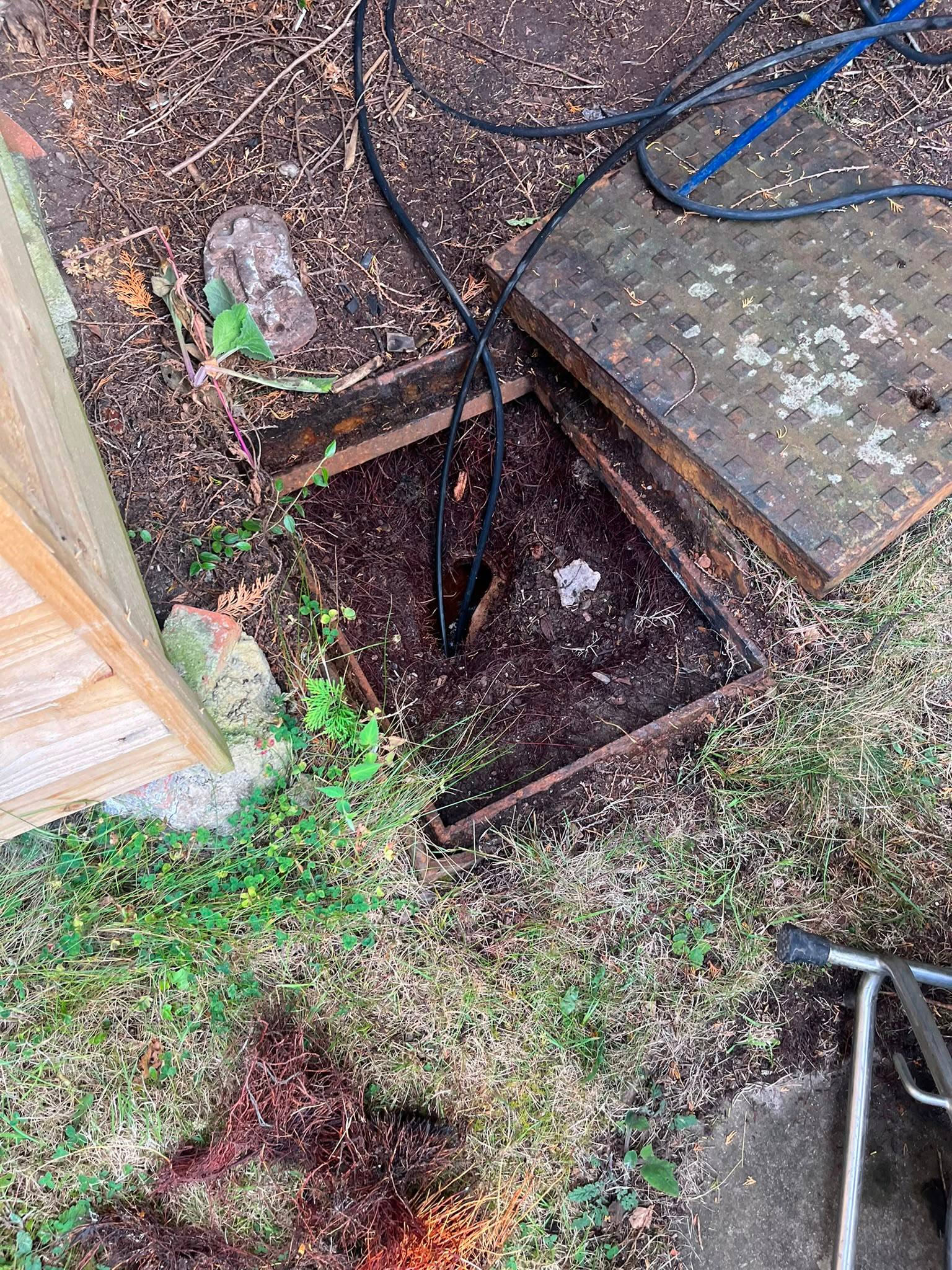 Open manhole revealing severe tree root ingress in a drain pipe being cleared by equipment