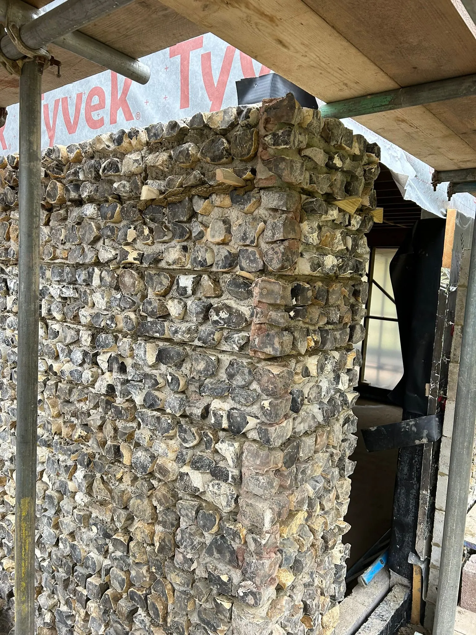Expert traditional flint and brick masonry wall under construction by professional bricklayers.