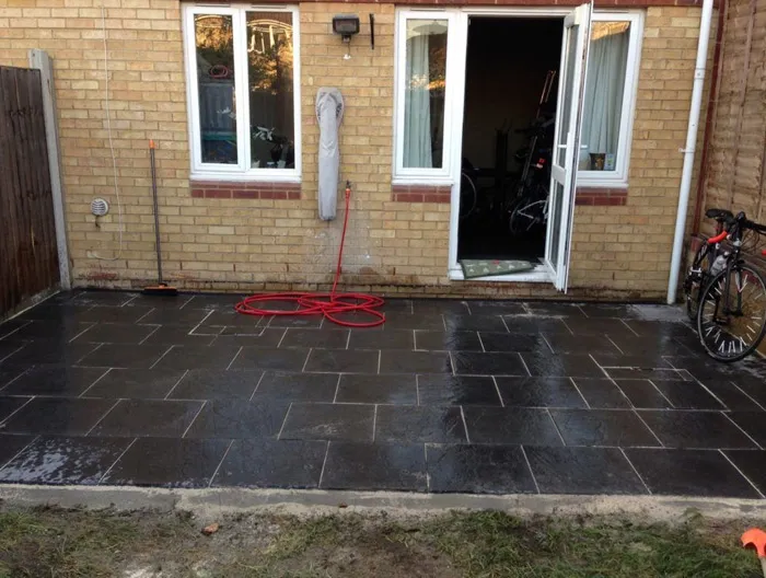 A new dark grey slab patio installed outside a brick house, featuring a sleek, wet surface and connecting to French doors.