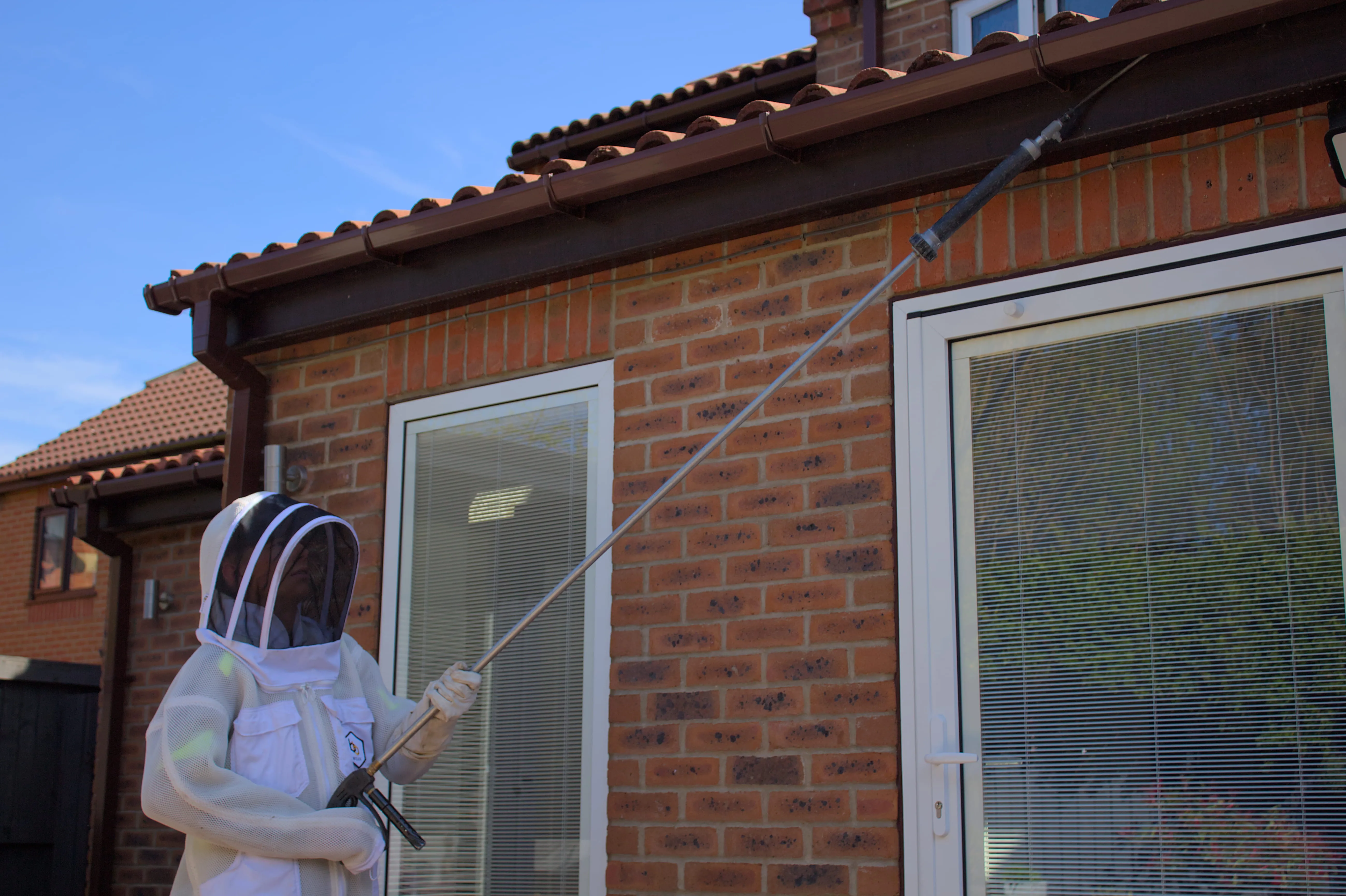 Professional wasp nest removal in Harrogate being carried out by a technician in a protective suit using a long-reach pole.