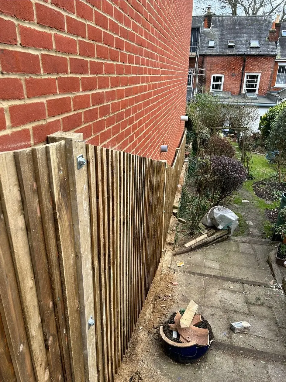 Newly installed stepped wooden garden fencing alongside a red brick house wall