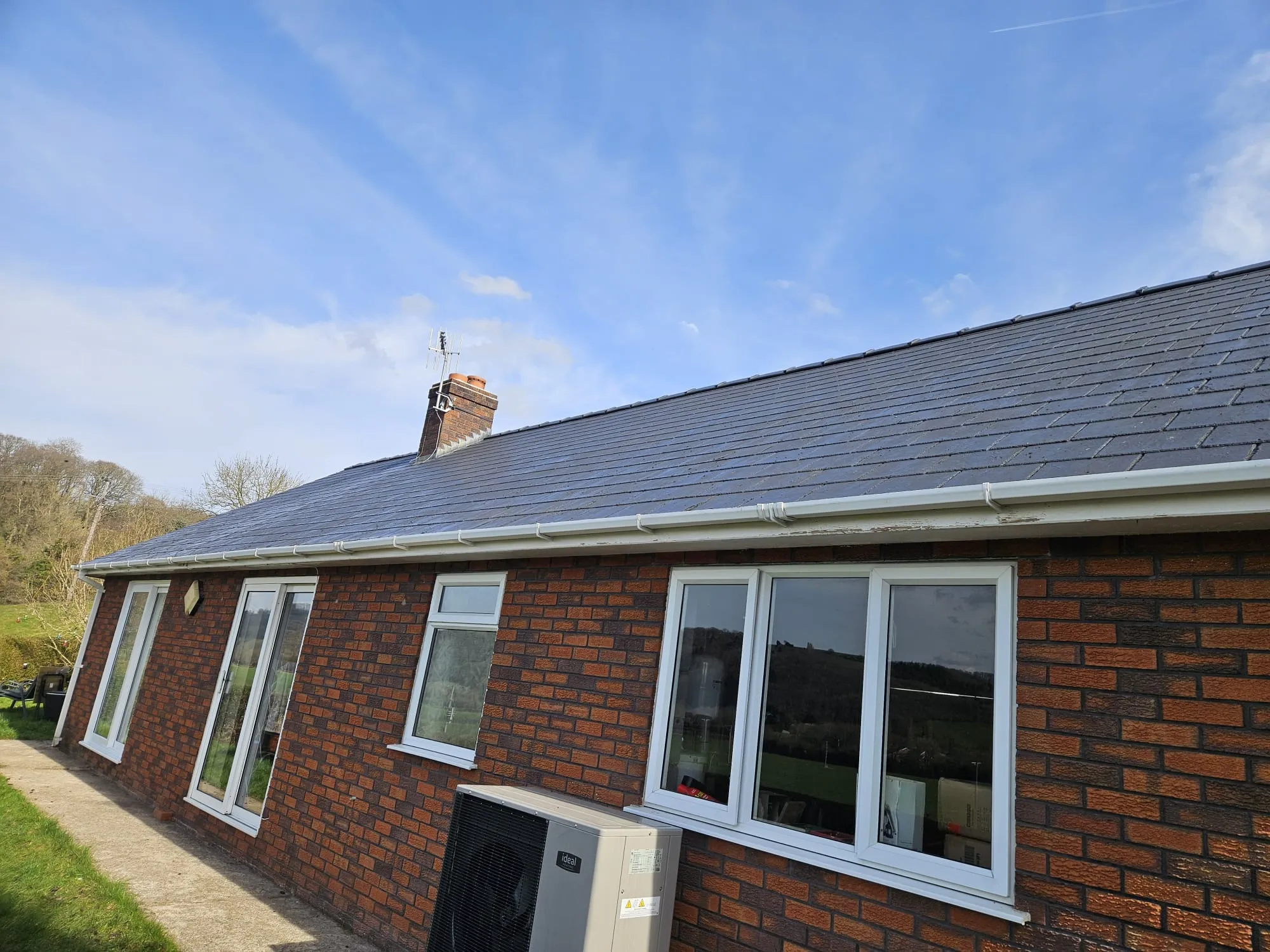 A modern brick house exterior showing a newly installed dark tiled roof with pristine white UPVC fascias, soffits, and guttering, and a brick chimney.