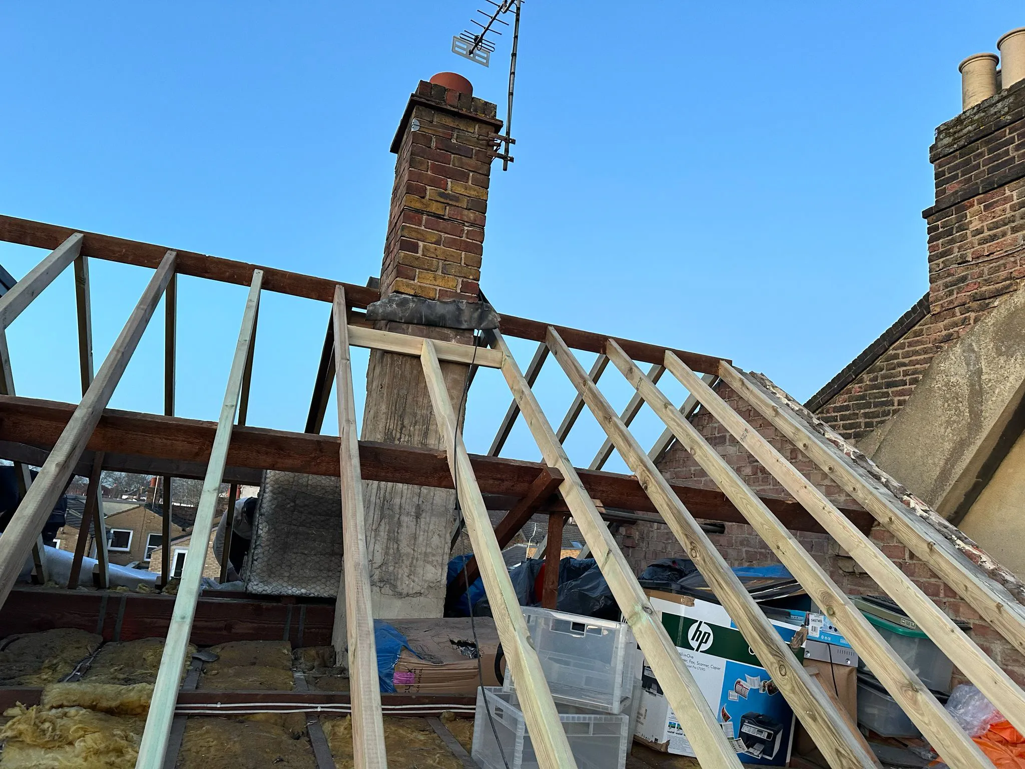 Treated timber roof rafters being installed on an open pitched roof frame next to a brick chimney