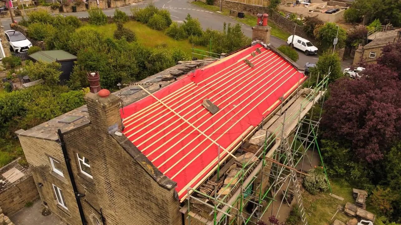 A pitched re-roofing project in progress on a stone building using red breathable membrane and timber battens.