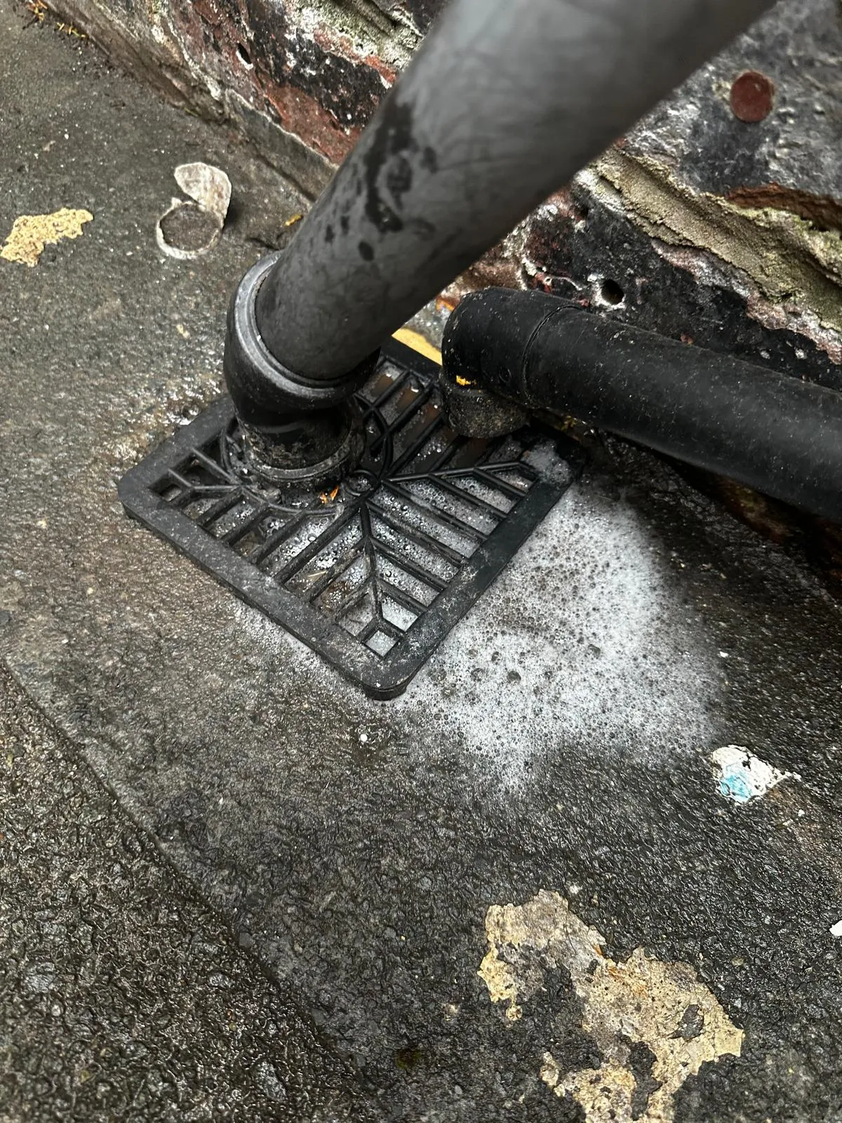 An overflowing external drain gully with white foam, showing a blocked drain issue.