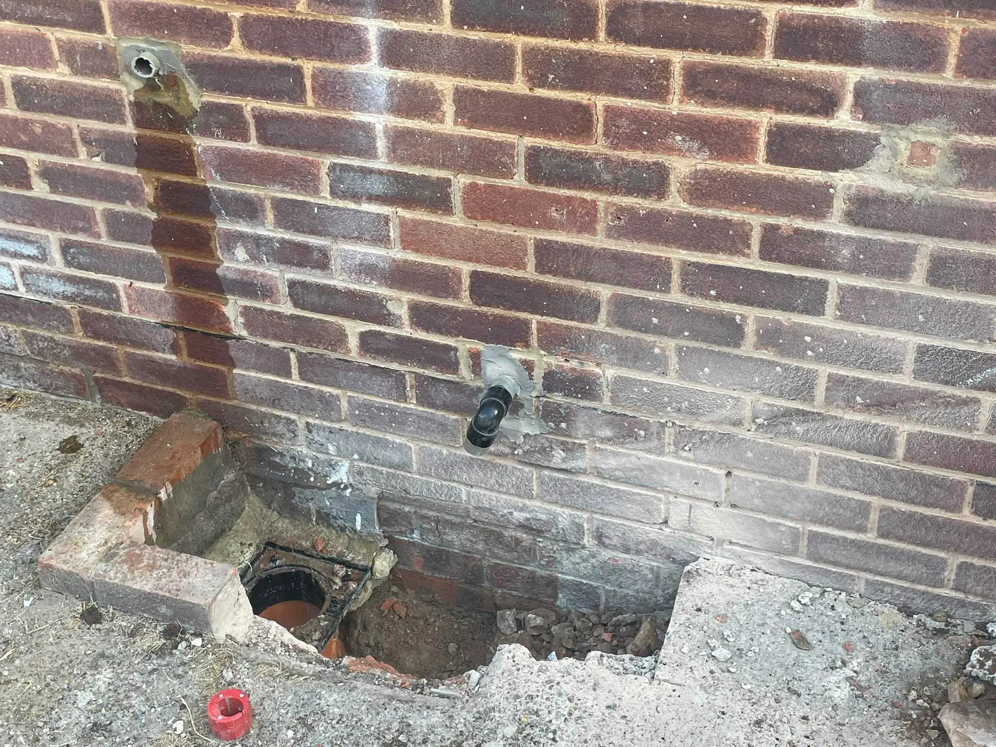 Water stain on an exterior brick wall from a leaking pipe above an open outside drain