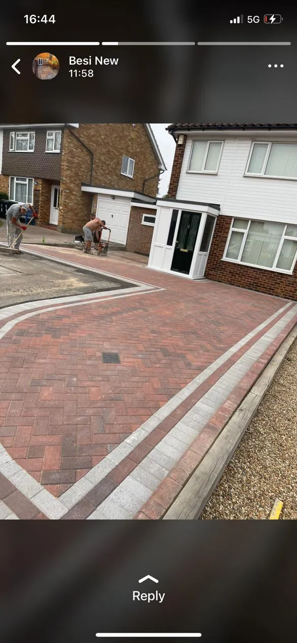 Two workers installing a block paved driveway with red and grey pavers in a herringbone pattern for a residential property.