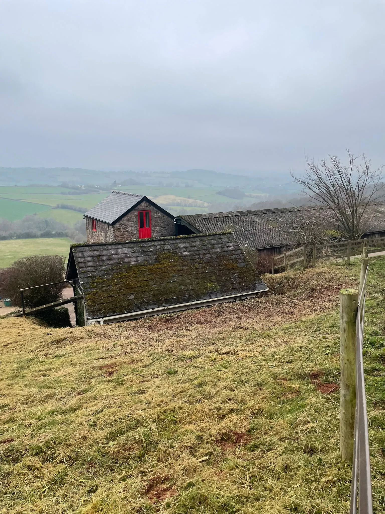 Sloping rural hillside property with post fencing overlooking valley buildings in South Wales