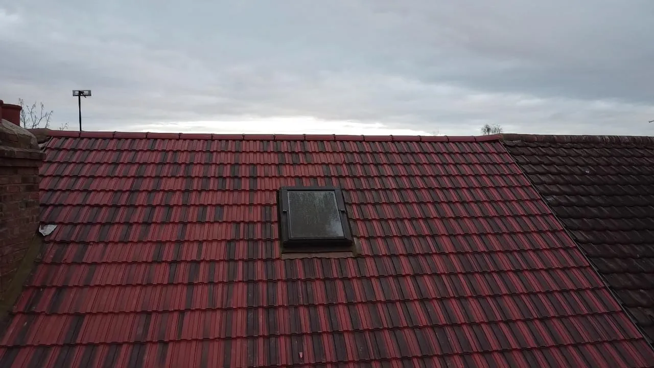 A modern tiled roof in red and dark red, showcasing a recently installed Velux window, with an older roof section visible next to it.