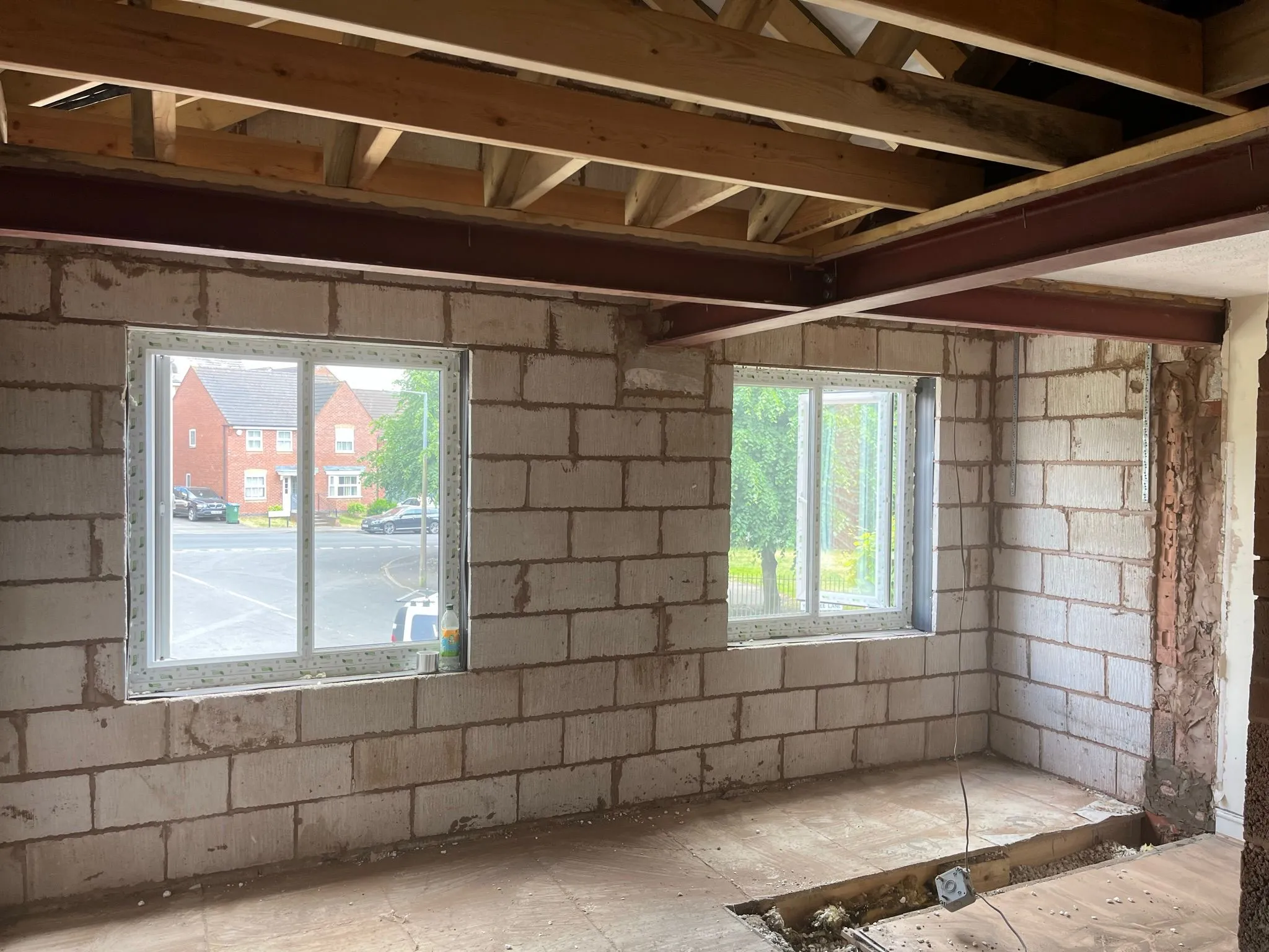Interior of a home extension during construction, featuring grey block walls, new white windows, and exposed wooden joists with steel beams overhead.