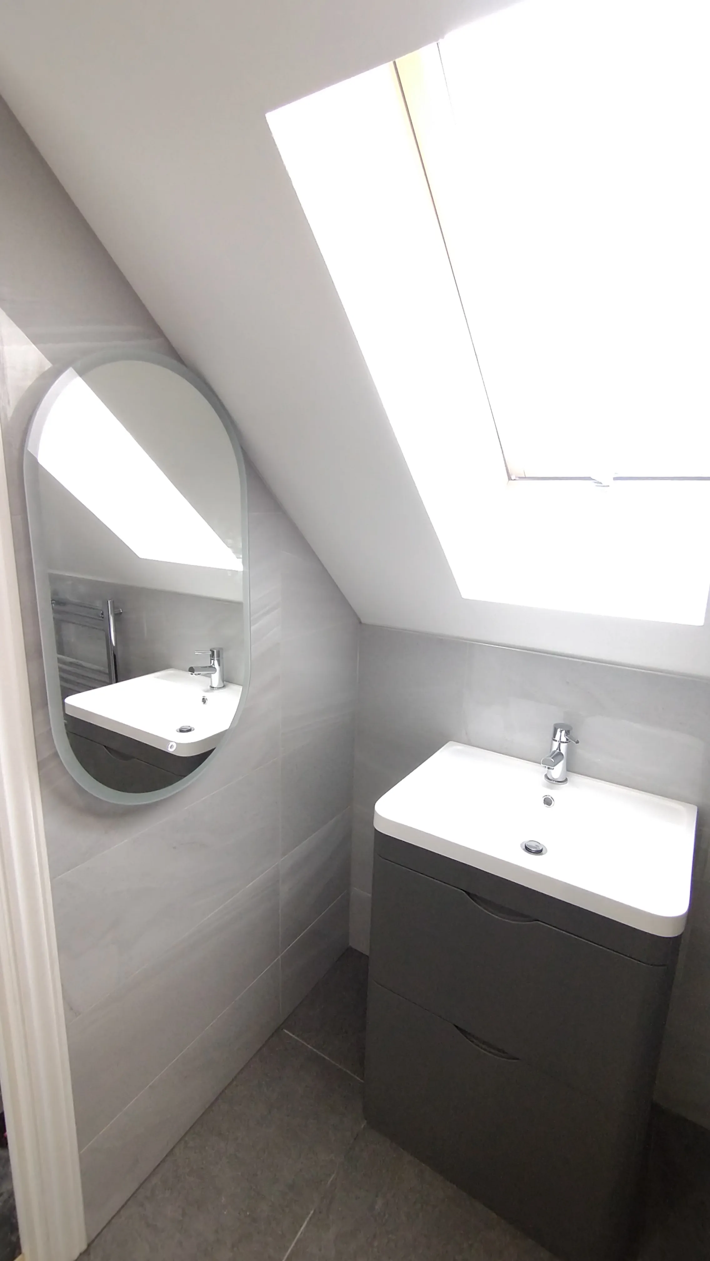 Luxury bespoke bathroom design and full installation in a Plymouth loft conversion featuring a modern vanity and oval mirror.