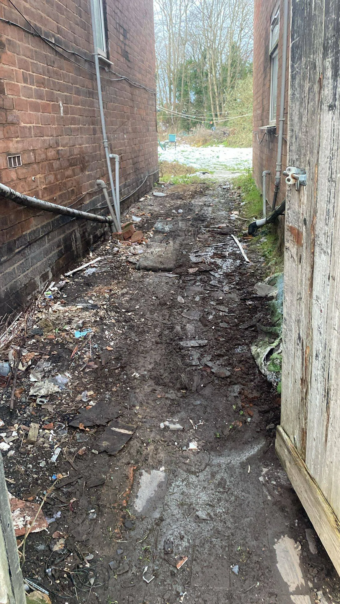 Debris, mud, and rubbish scattered along a narrow side alley between two brick houses before clearance