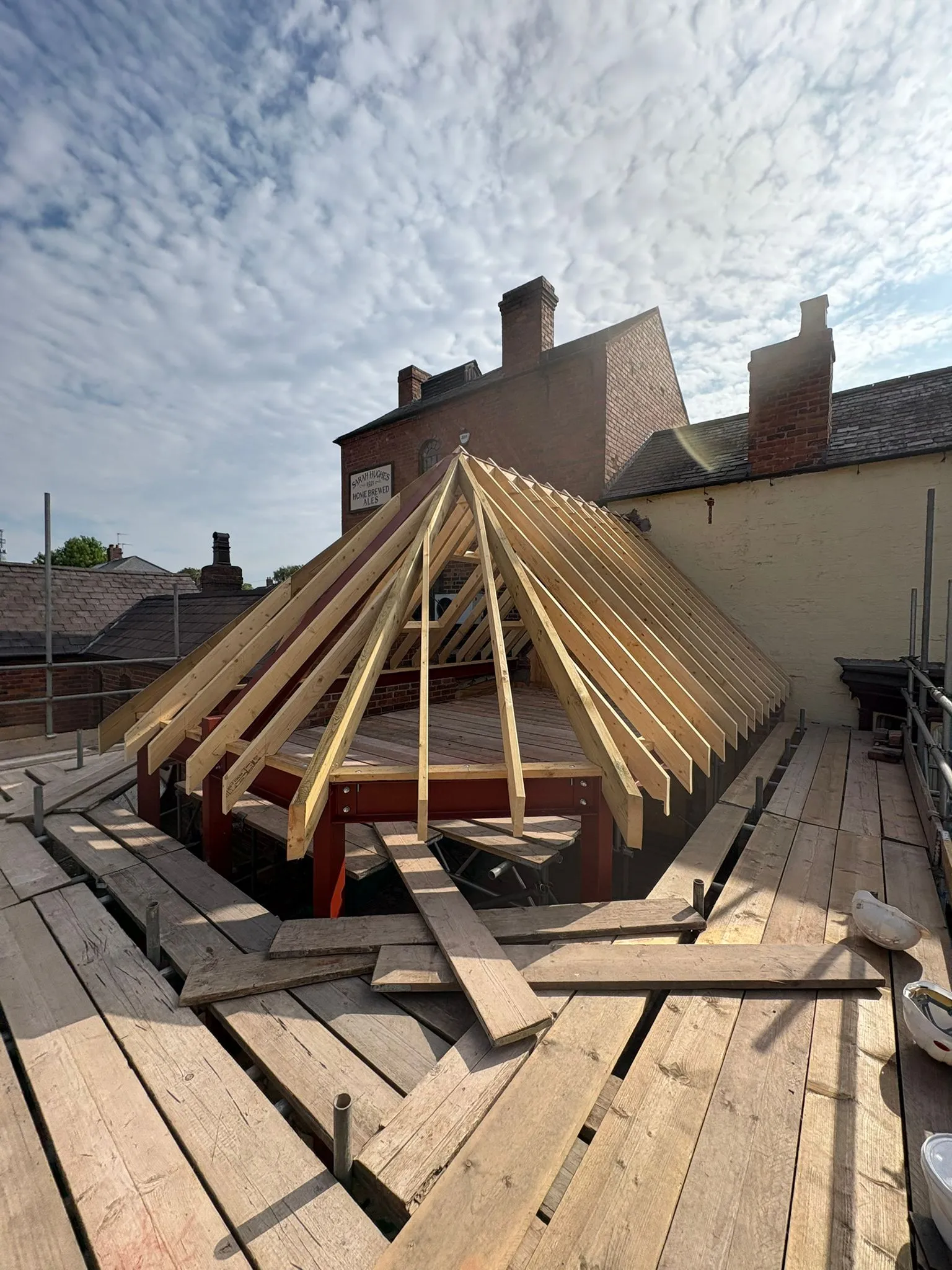 Home extension under construction with exposed timber roof rafters and scaffolding on a sunny day.