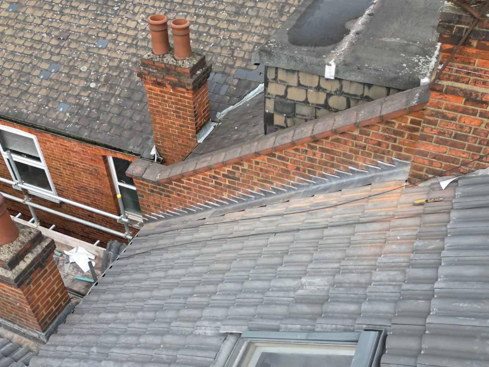 Complex residential roof with new grey tiles, brick chimneys, lead flashing, and a roof window.