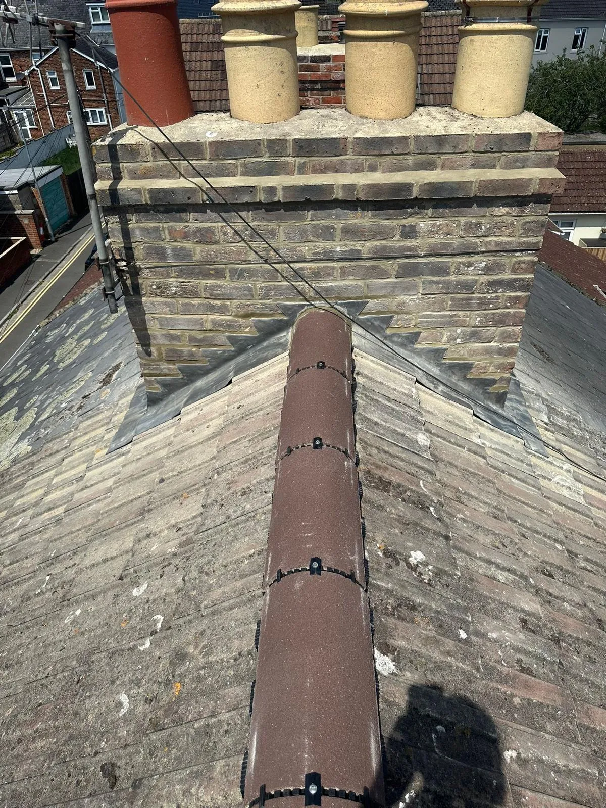A residential roof with a brick chimney, lead flashing, and a modern dry ridge system.