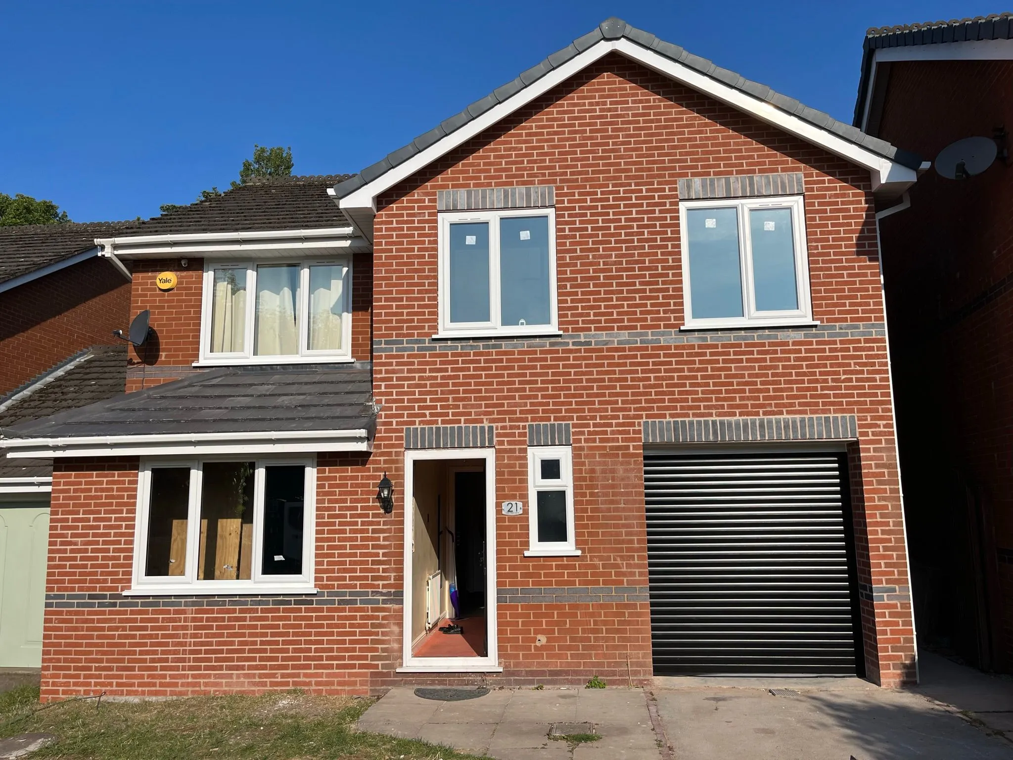 Front exterior of a modern red brick house with a black garage door and new white windows, under a clear blue sky.