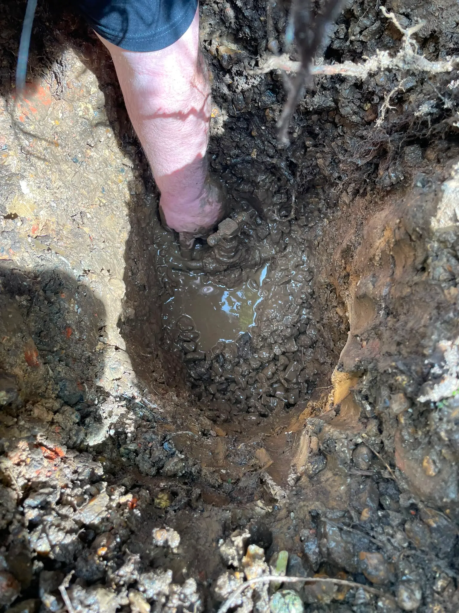 Plumber from Local Plumbing & Drainage repairing an underground pipe in a muddy trench