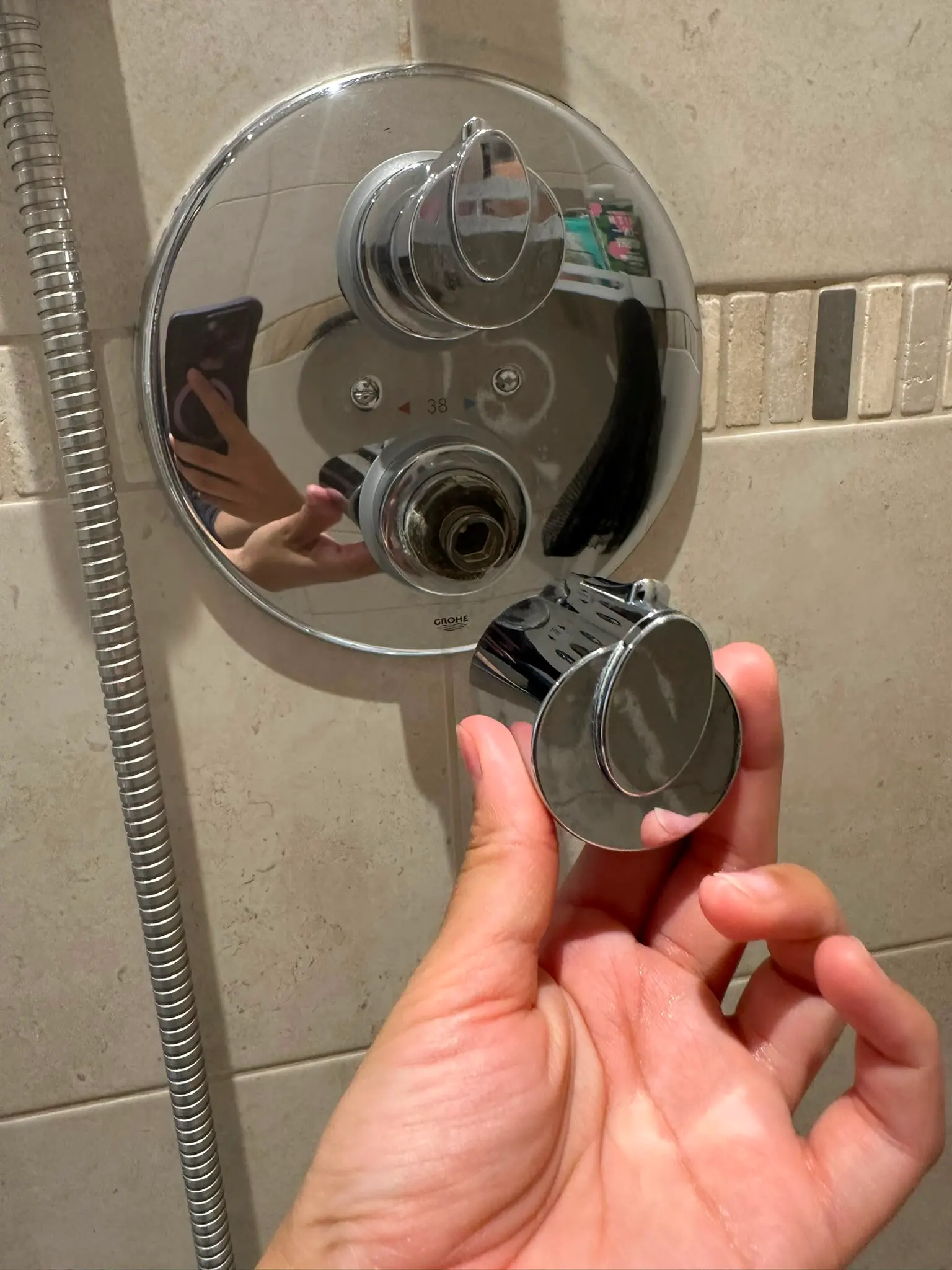 A broken chrome shower mixer valve with a detached knob held in a hand
