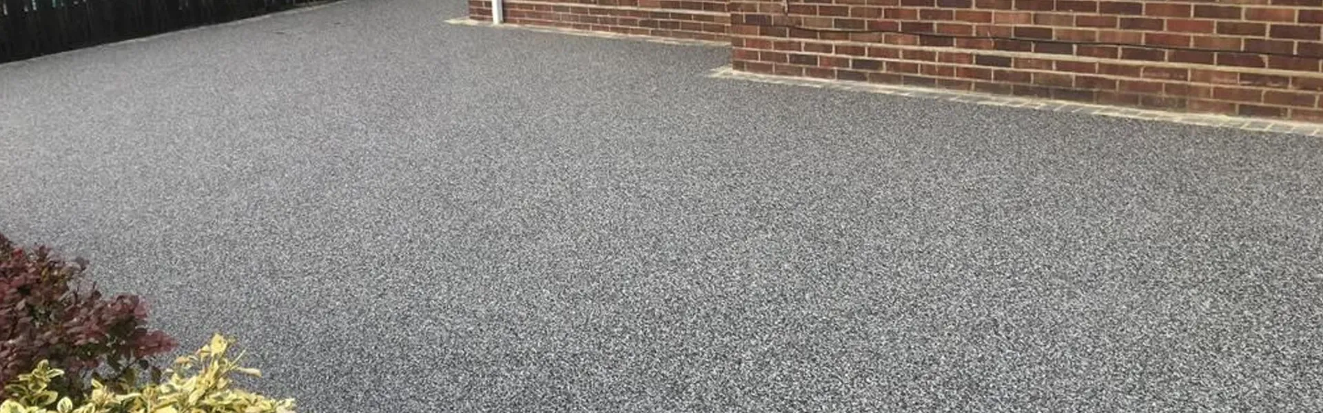 A modern grey resin-bound driveway leading up to a red brick residential property.