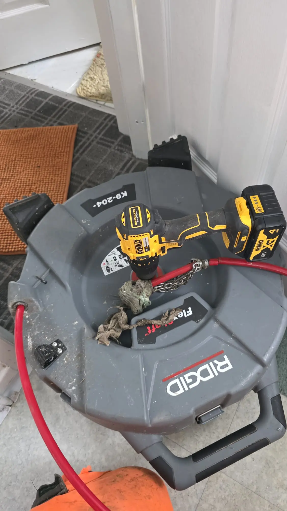 A Ridgid FlexShaft mechanical drain unblocking machine powered by a DeWalt cordless drill, showing debris removed from a pipe.