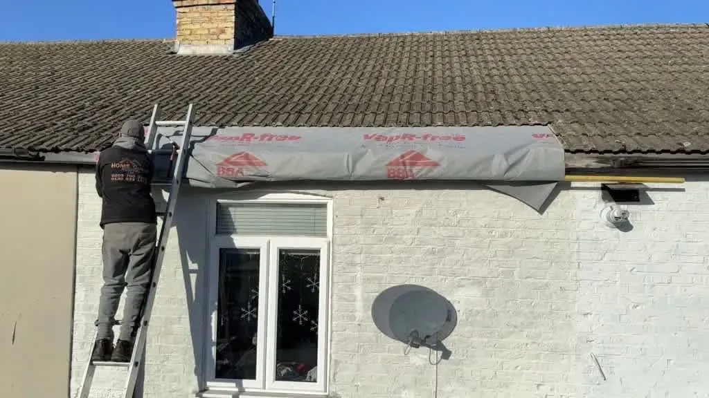 A HomeGuard Roofing Ltd roofer on a ladder fitting a grey VapR-free roofing underlay membrane to the lower section of a tiled roof.
