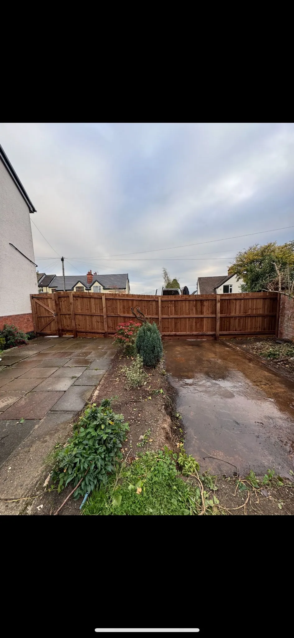 Newly installed wooden garden fence and gate, showing a paved area and cleared ground ready for a landscaping project.