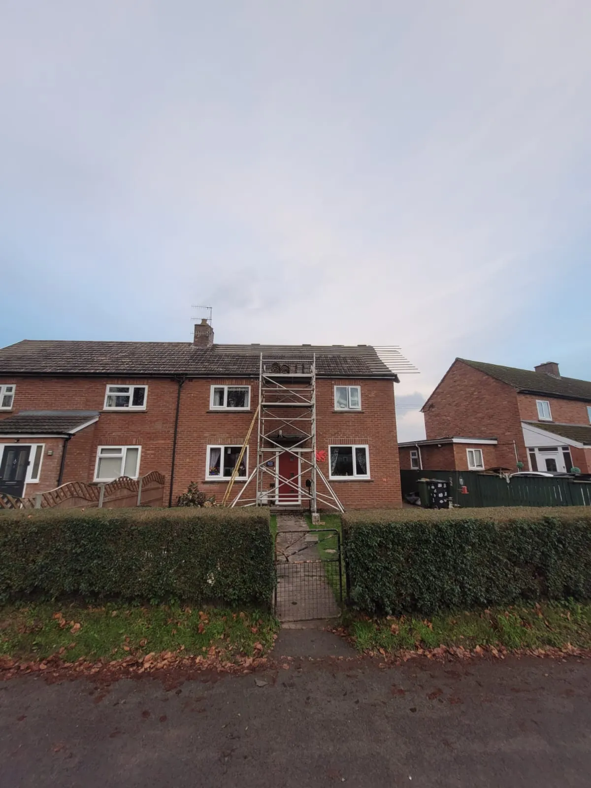 A semi-detached brick house undergoing a roof replacement with scaffolding, showing exposed roof battens and missing roof tiles.