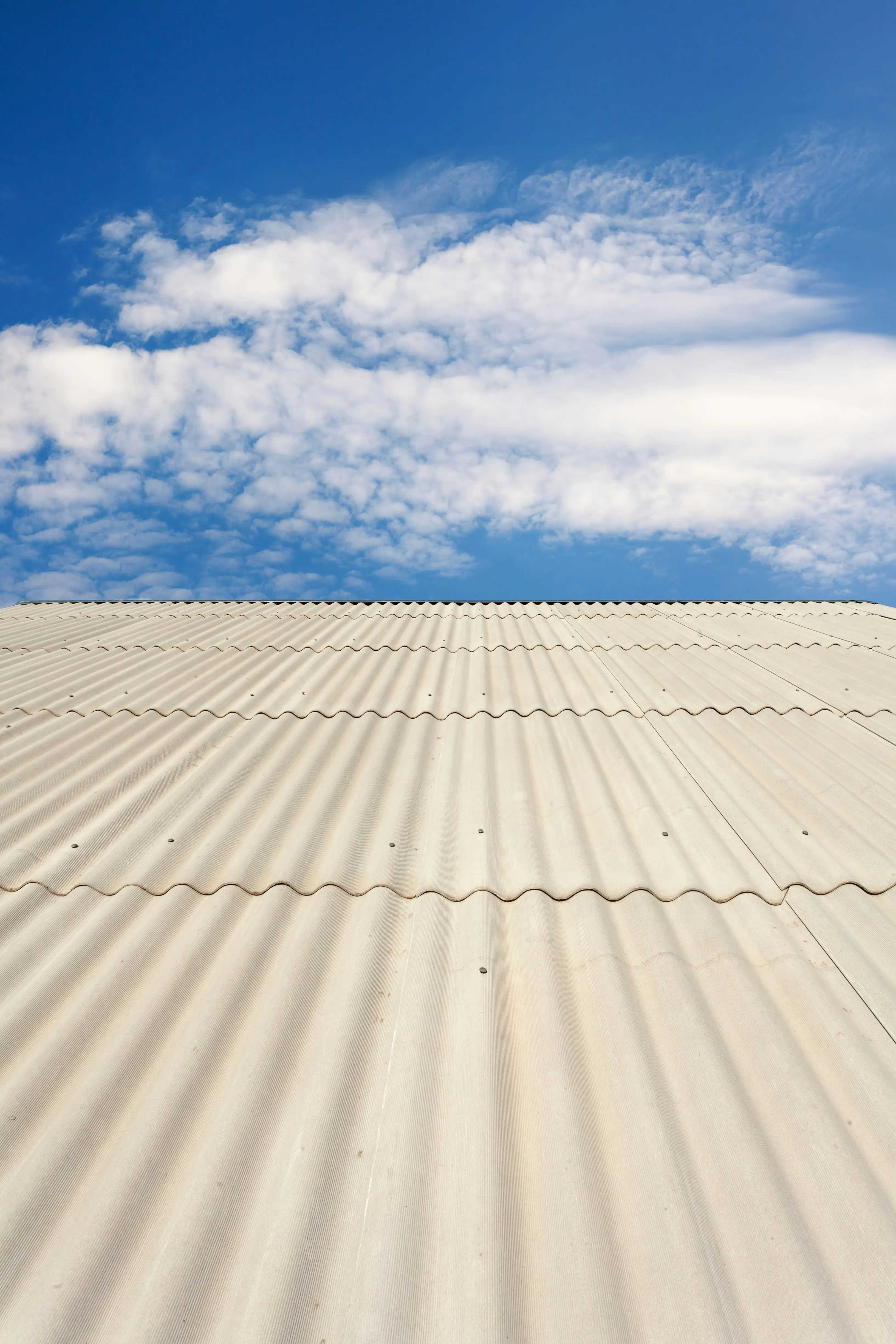 Corrugated asbestos cement roof on a garage or outbuilding under a blue sky, indicating a need for professional asbestos removal.