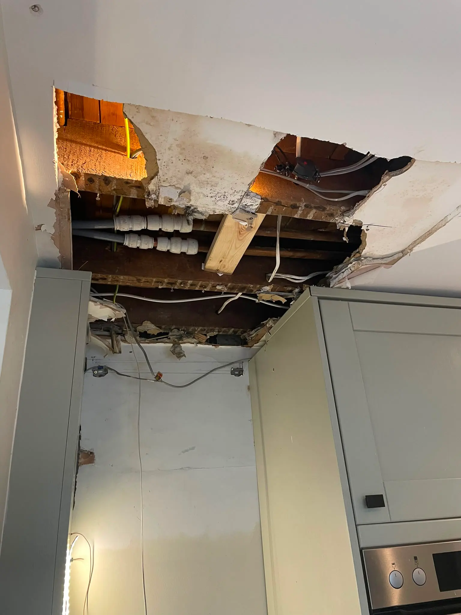 Damaged kitchen ceiling exposing plumbing pipes and joists due to a hidden water leak