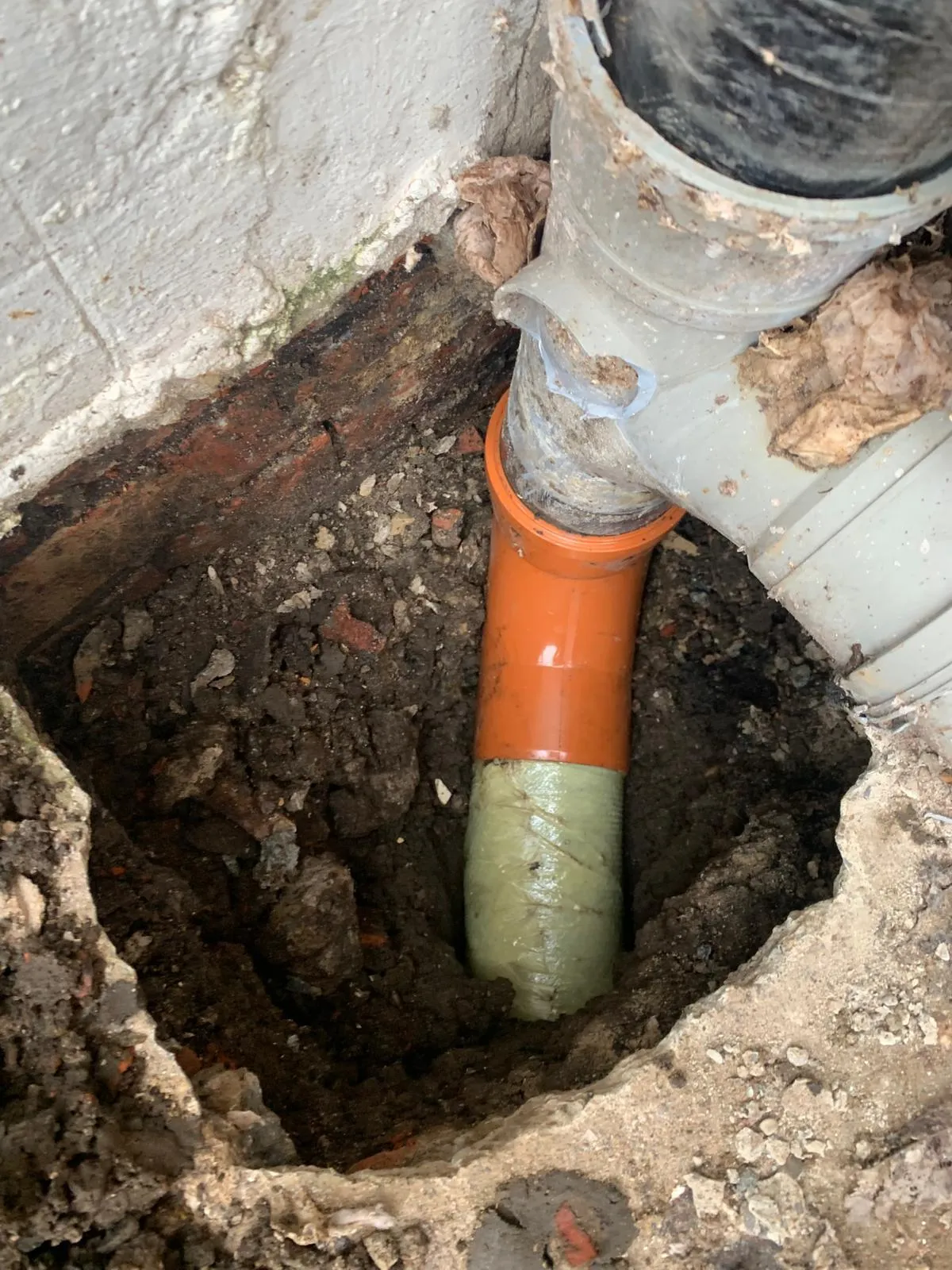 A professional drain relining repair in Durham, showing a new pipe liner and orange plastic connection within an excavated access point.