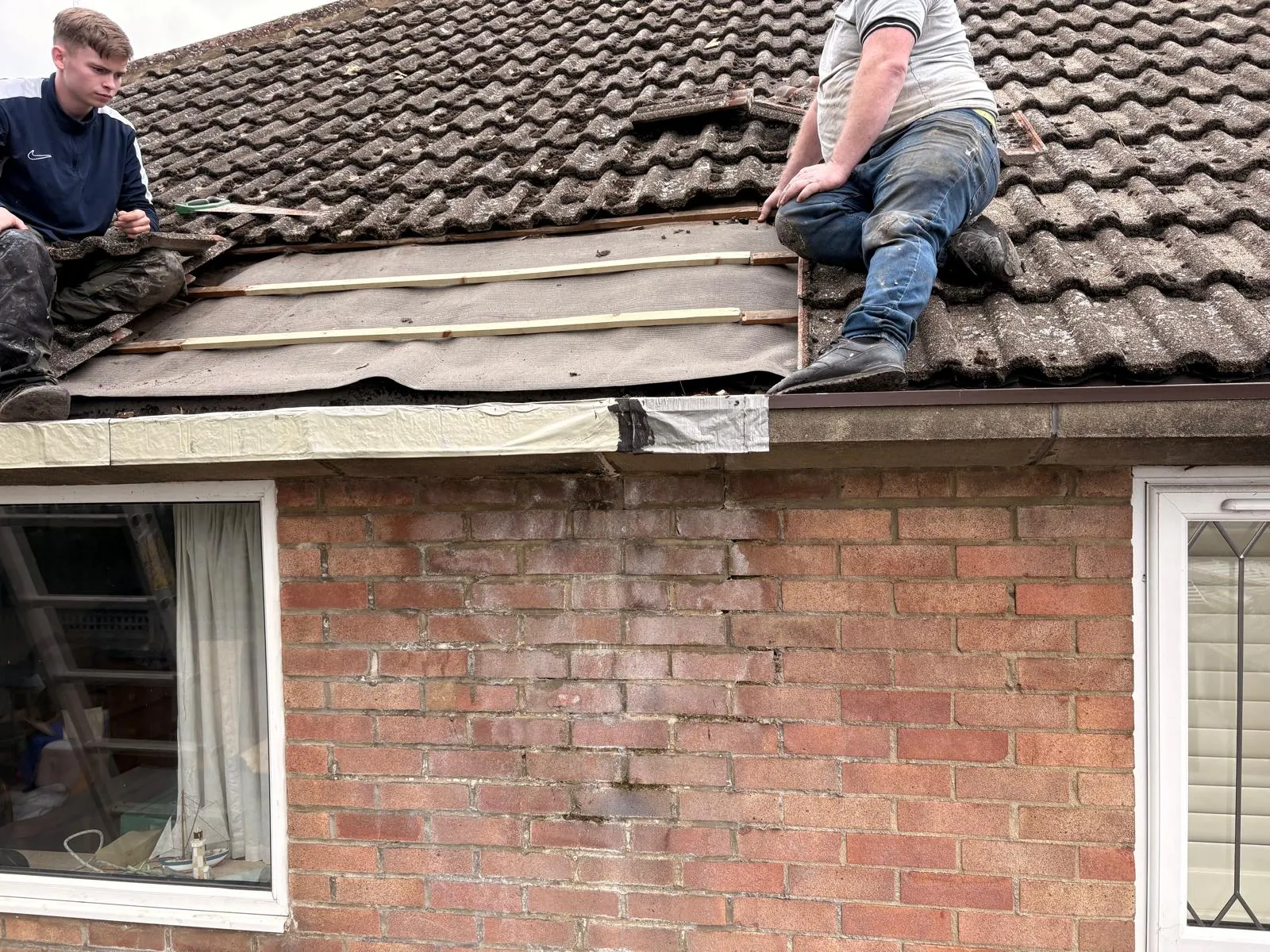 Roofers repairing underlay membrane and timber battens on a pitched concrete tile roof