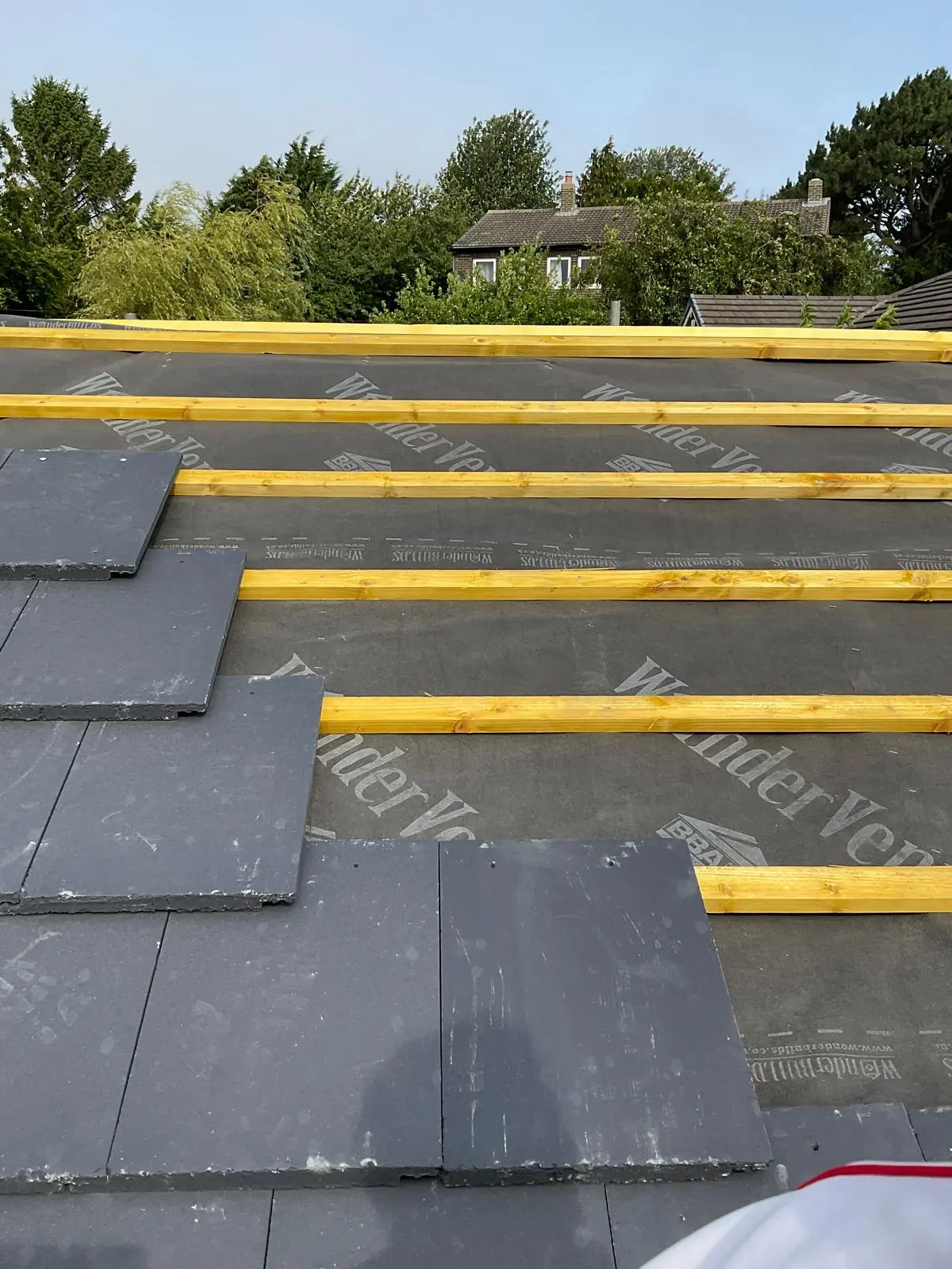 Close-up of a pitched roof installation in progress with grey tiles, timber battens, and breathable underlay