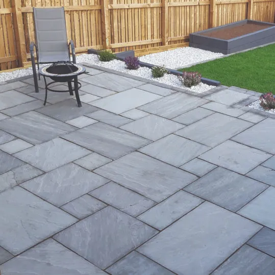 A modern grey paving slab patio with garden furniture, set in a neat garden with a lawn and wooden fence.