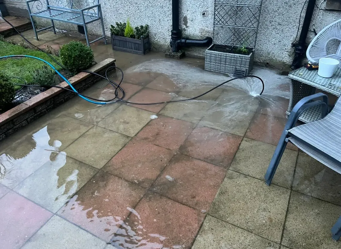 A tiled residential patio with standing water and a hose, showing a drainage issue or drain unblocking.