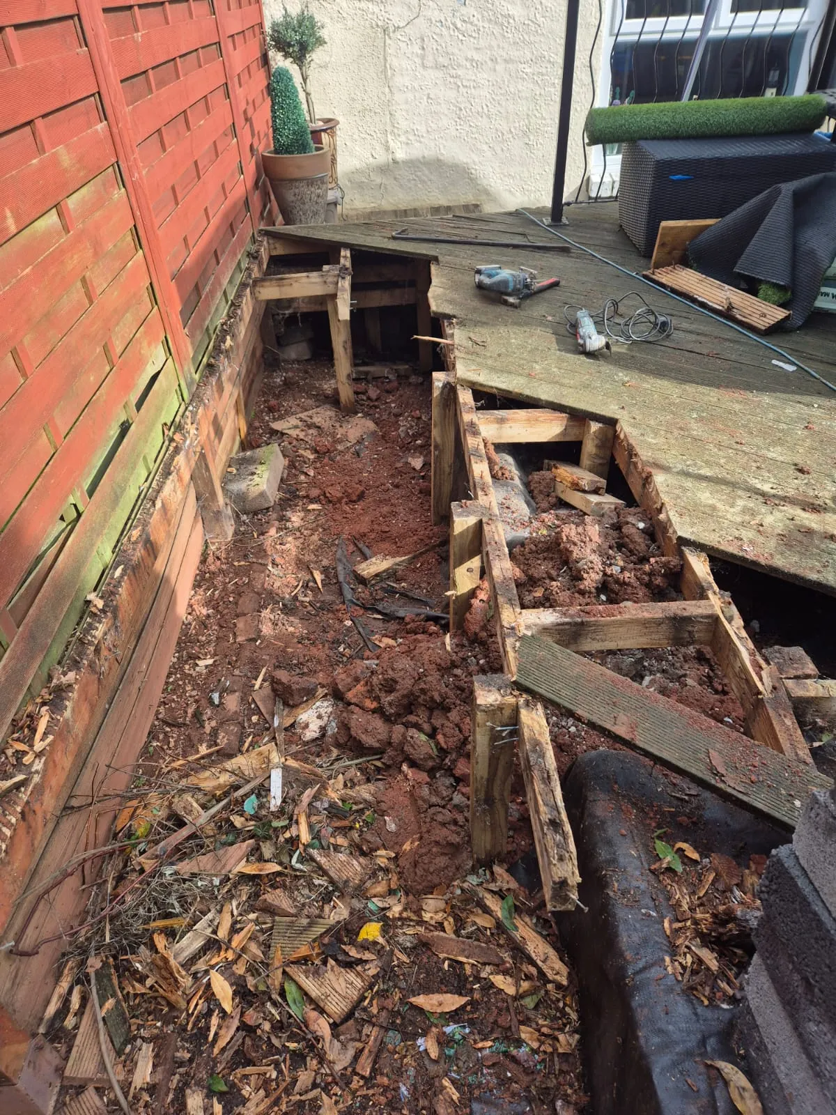 Groundworks in progress at a residential property, with exposed soil and remnants of removed decking.