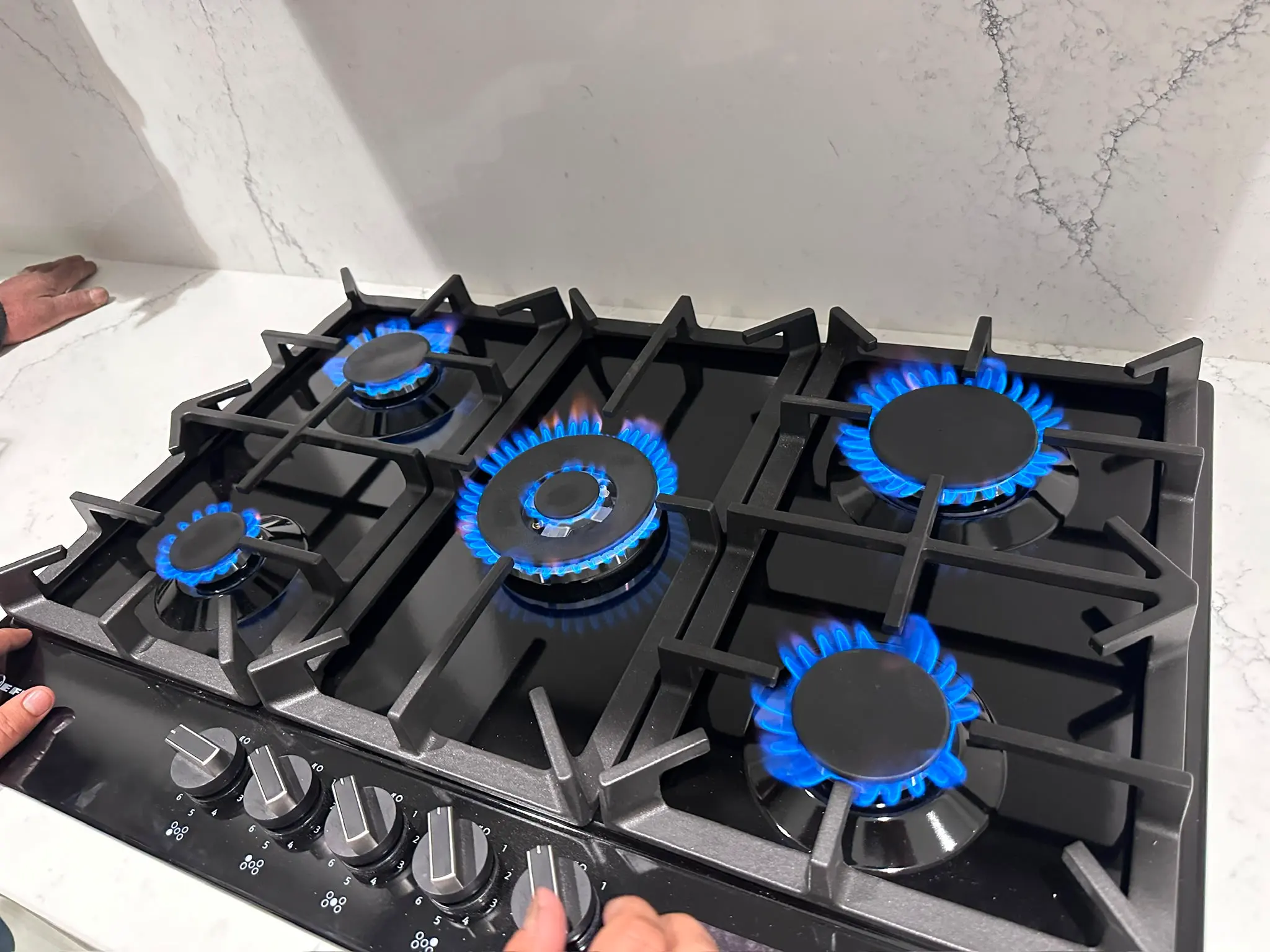A newly installed black glass gas hob with five lit burners being tested by a Gas Safe registered engineer in Snodland.