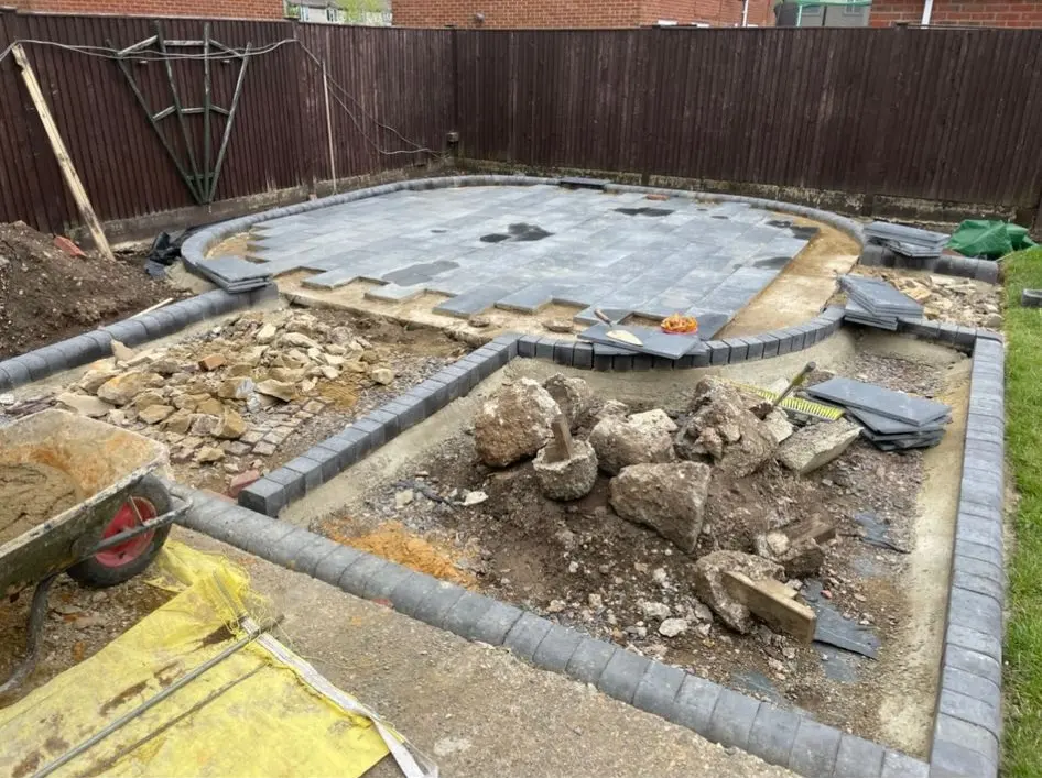 A work-in-progress shot of a new patio being installed in a garden, featuring grey slabs and dark edging blocks.